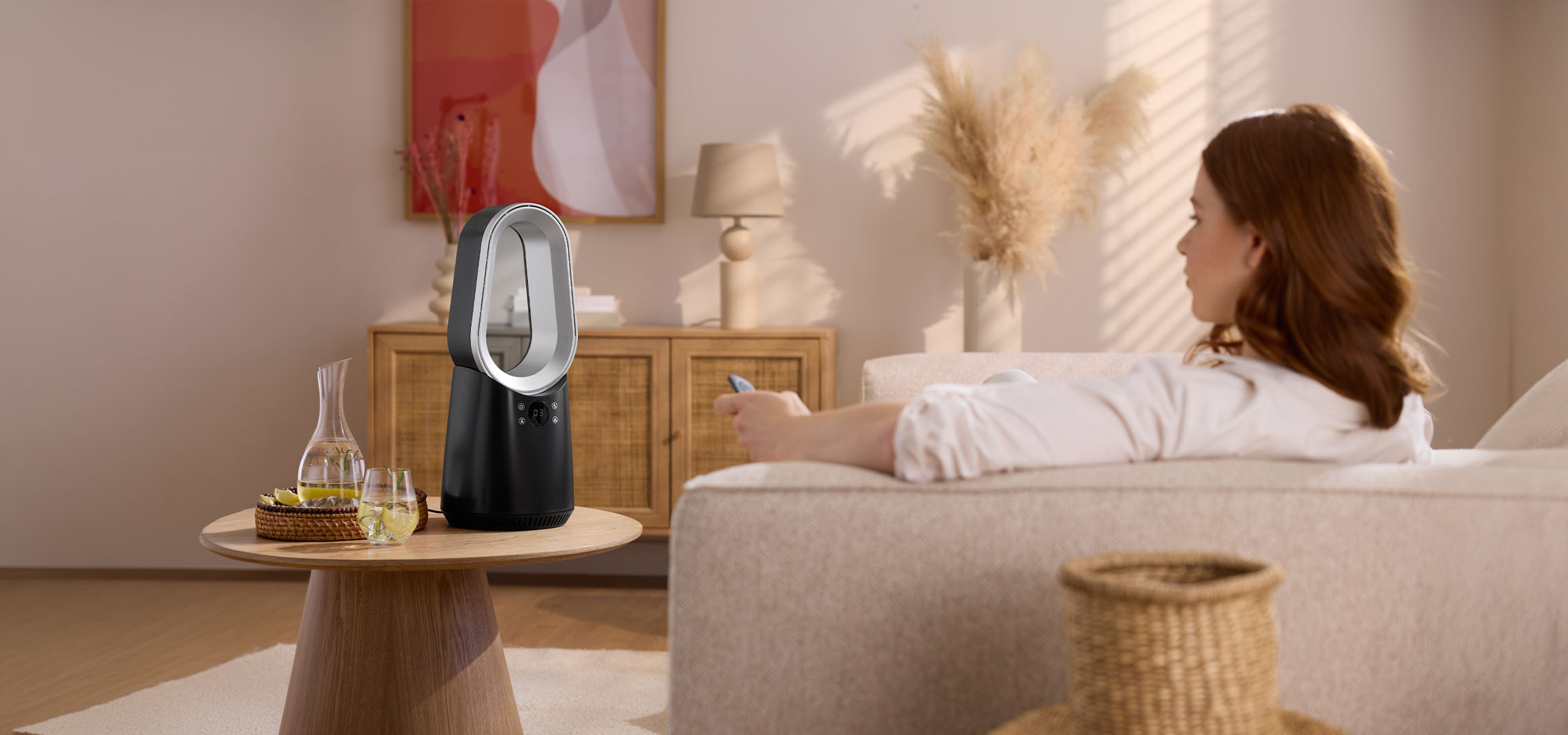 Ženska na kavču z daljincem, sodoben ventilator in pijače na mizi.