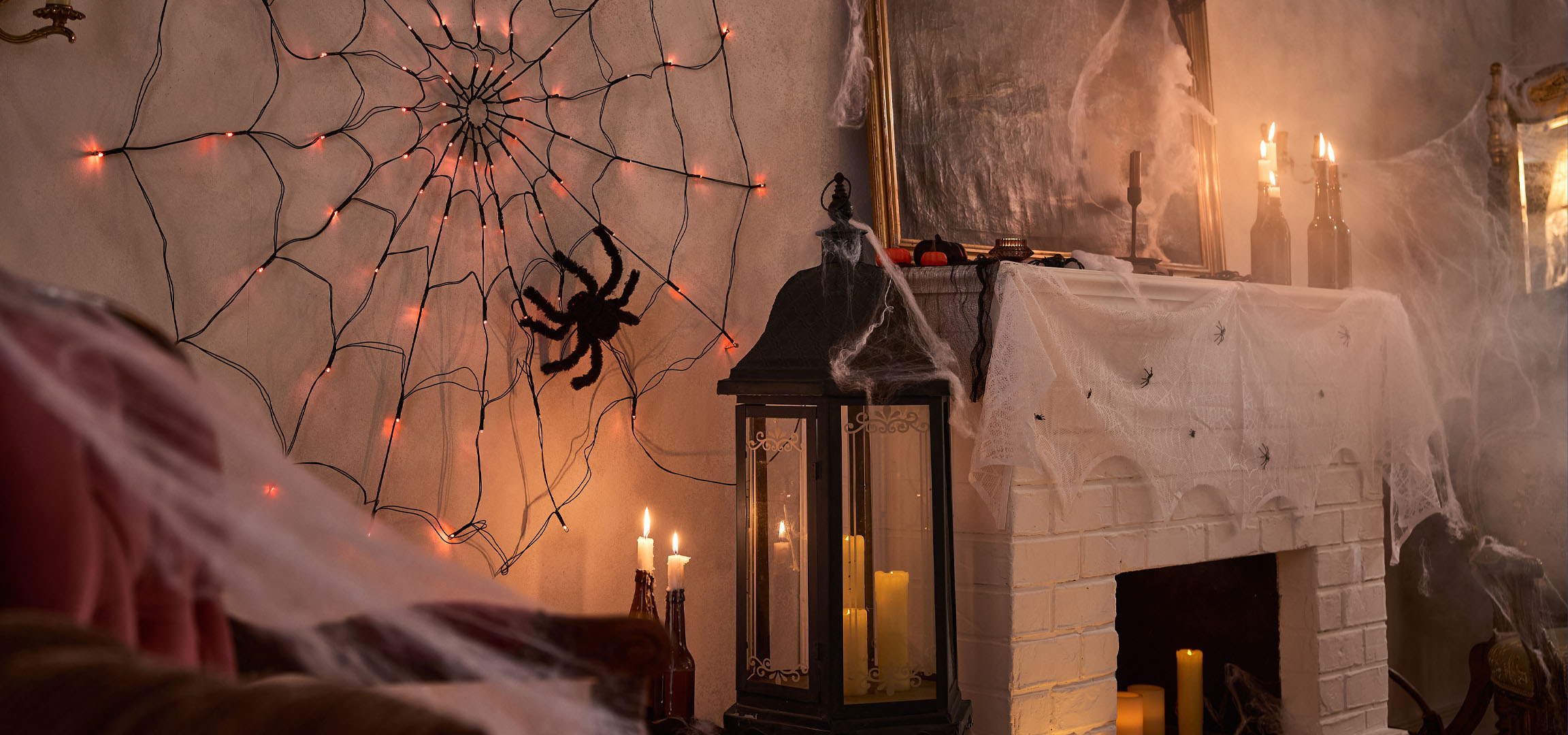 Halloweenske dekoracije s pajčevinastimi lučkami, velikim pajkom in svečami.