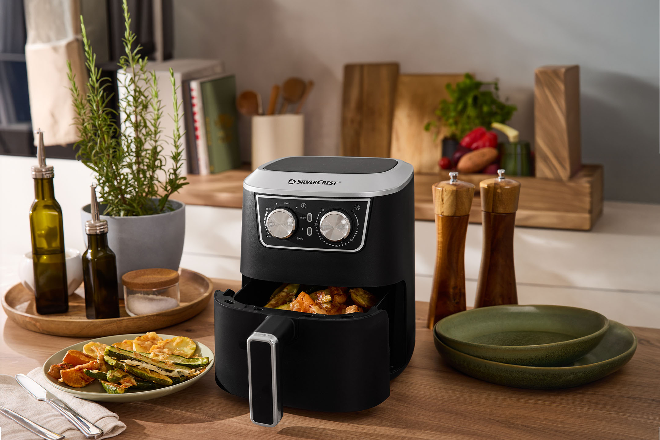 Črni cvrtnik na vroč zrak z zelenjavo, začimbami in posodo na leseni mizi.