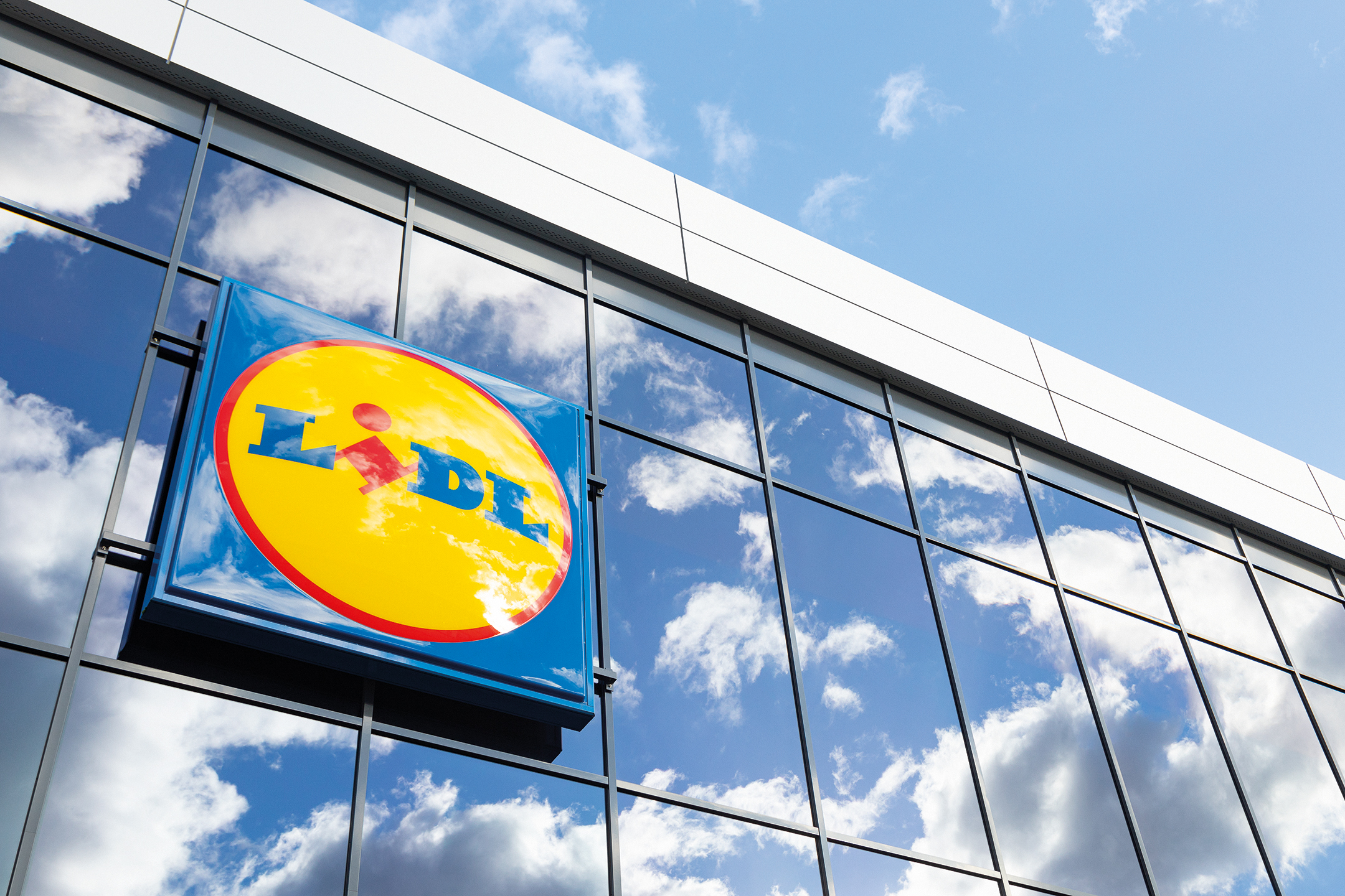 Lidl napis na stekleni fasadi stavbe, z odsevom neba in oblakov.