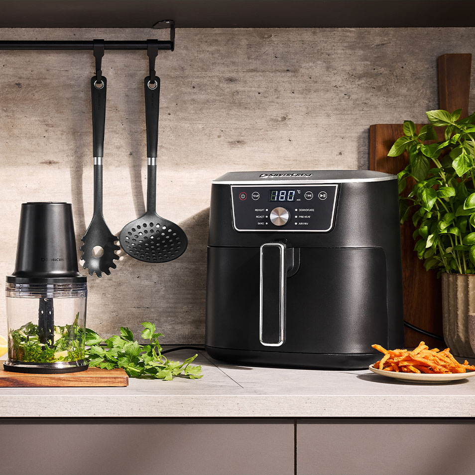 SilverCrest cvrtnik na vroč zrak in sekljalnik hrane na kuhinjskem pultu s svežimi zelišči in pomfritom iz sladkega krompirja.