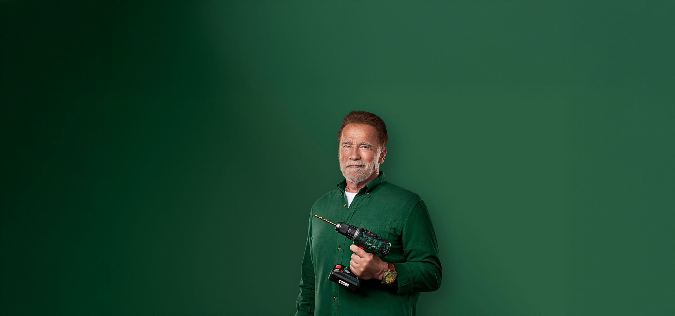 Arnold Schwarzenegger drži vrtalnik Parkside na zelenem ozadju.