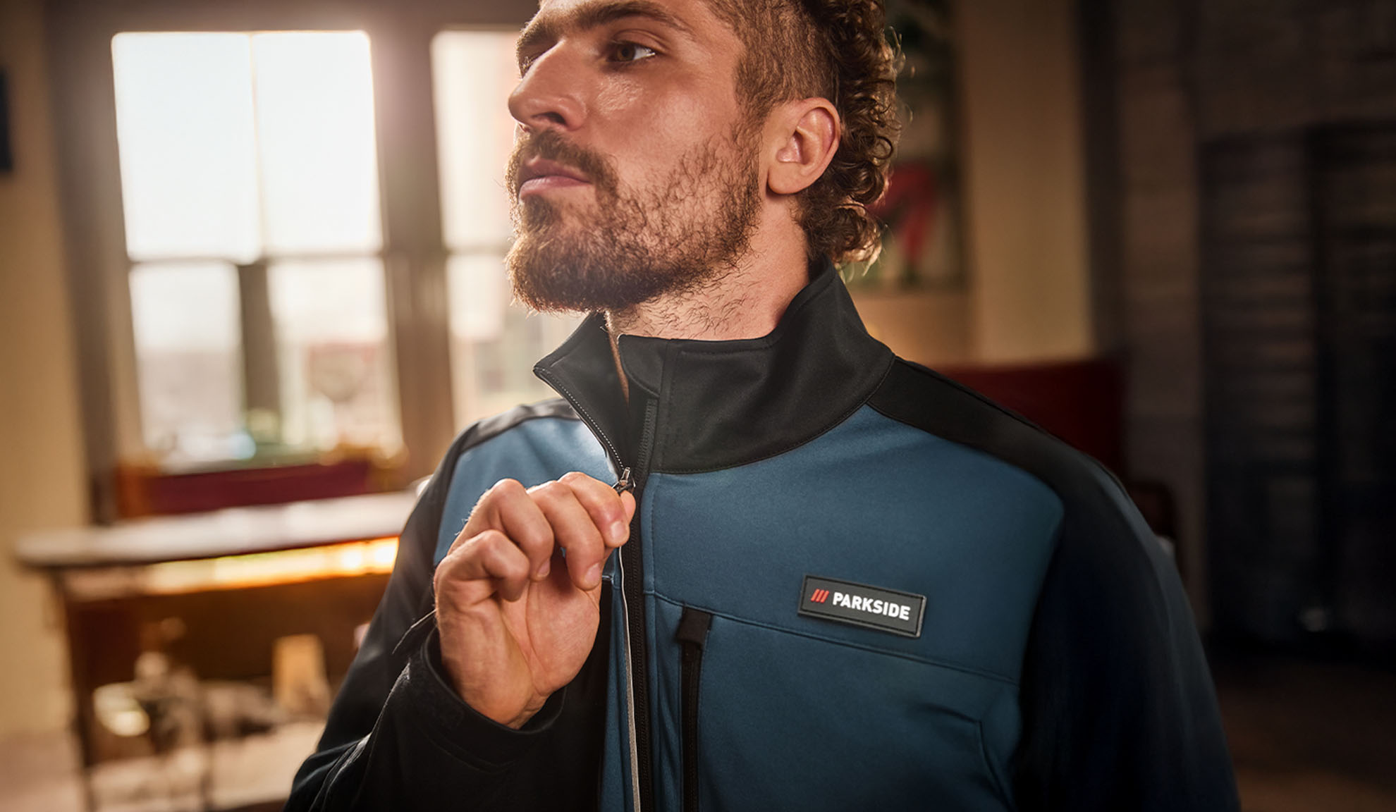Moški v modro-črni delovni jakni Parkside, ki jo zapenja.