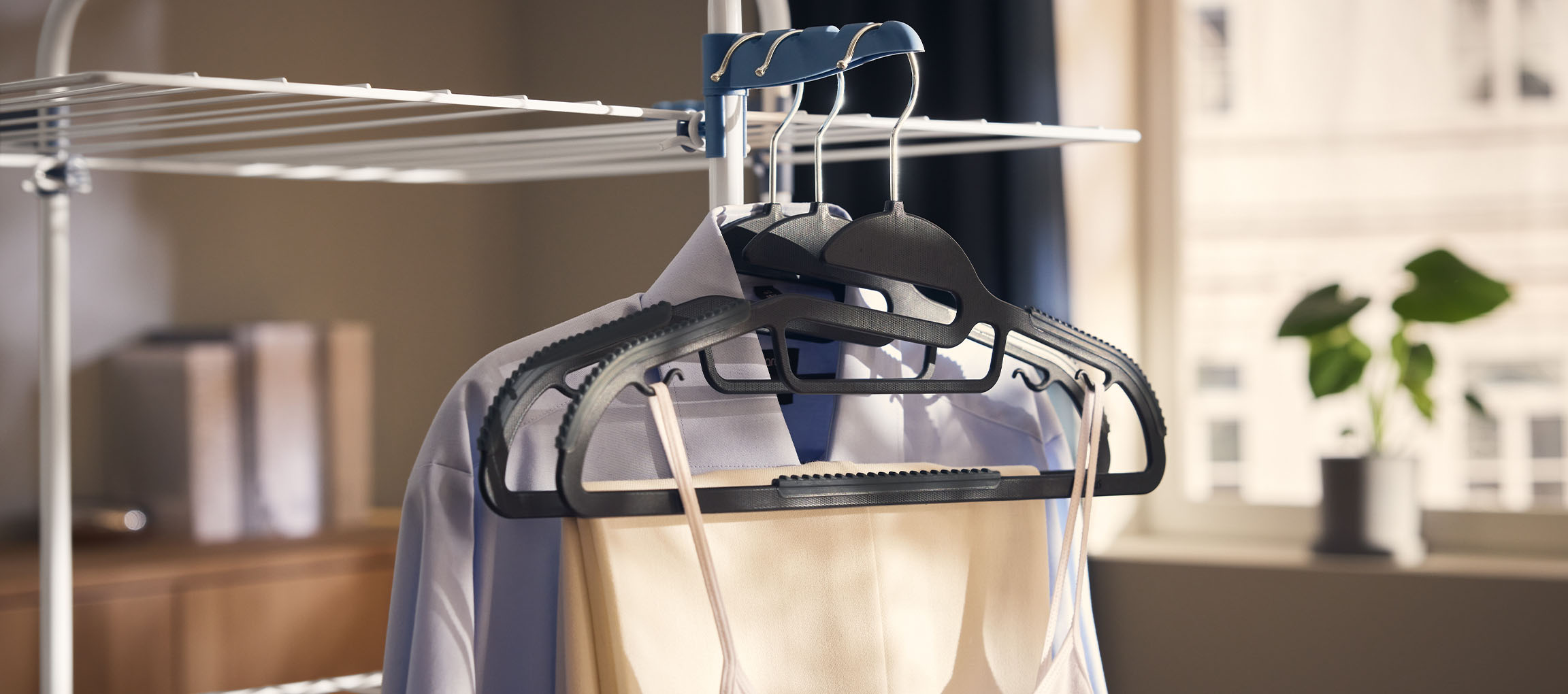 Oblačila na obešalnikih na sušilniku perila, z rastlino v ozadju.