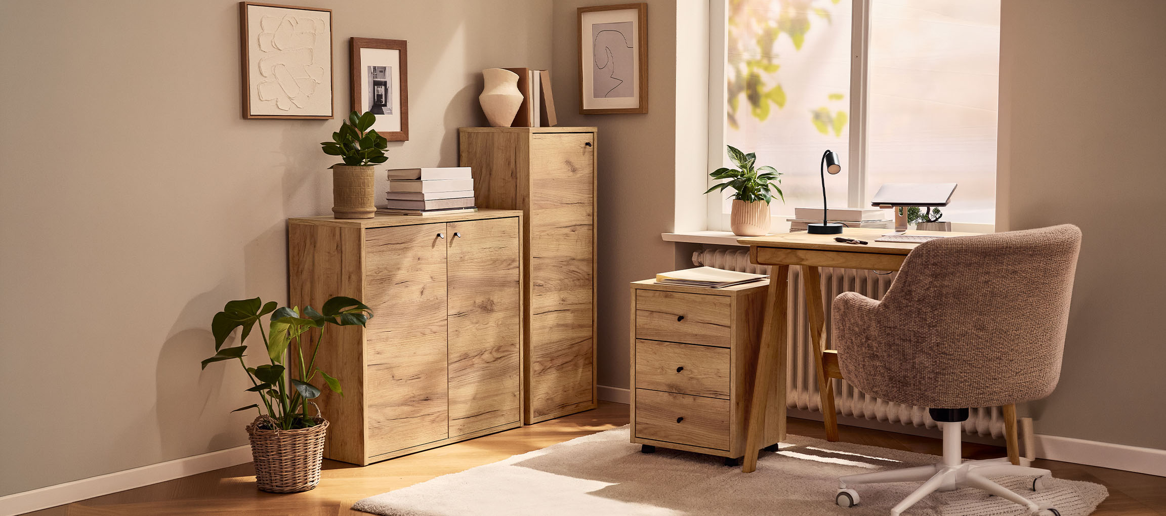 Domača pisarna z lesenimi omaricami, mizo in stolom, okrašena z rastlinami in slikami.