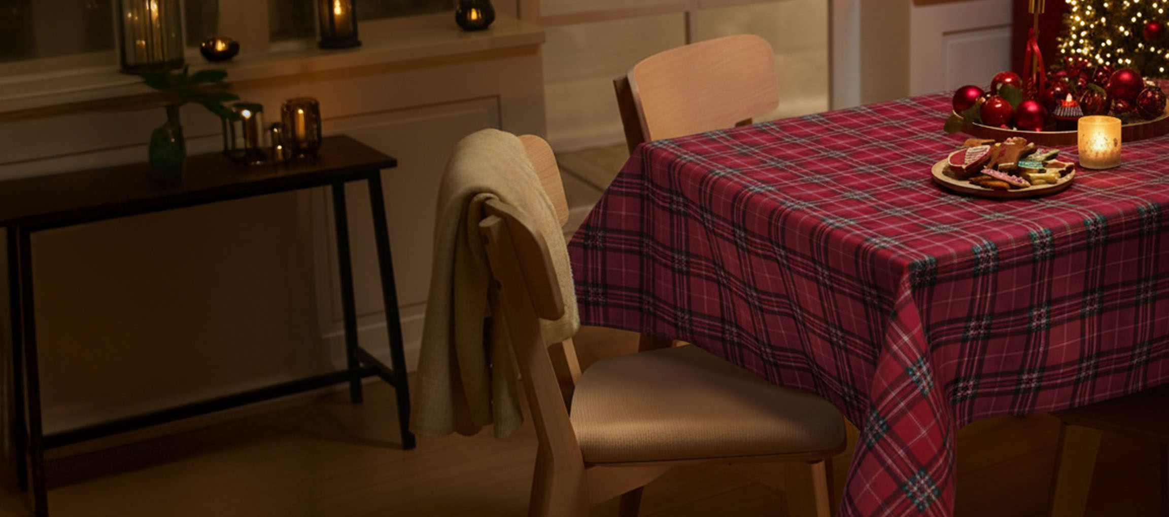 Božična miza z rdečim kariranim prtom, stoli in božičnimi piškoti.