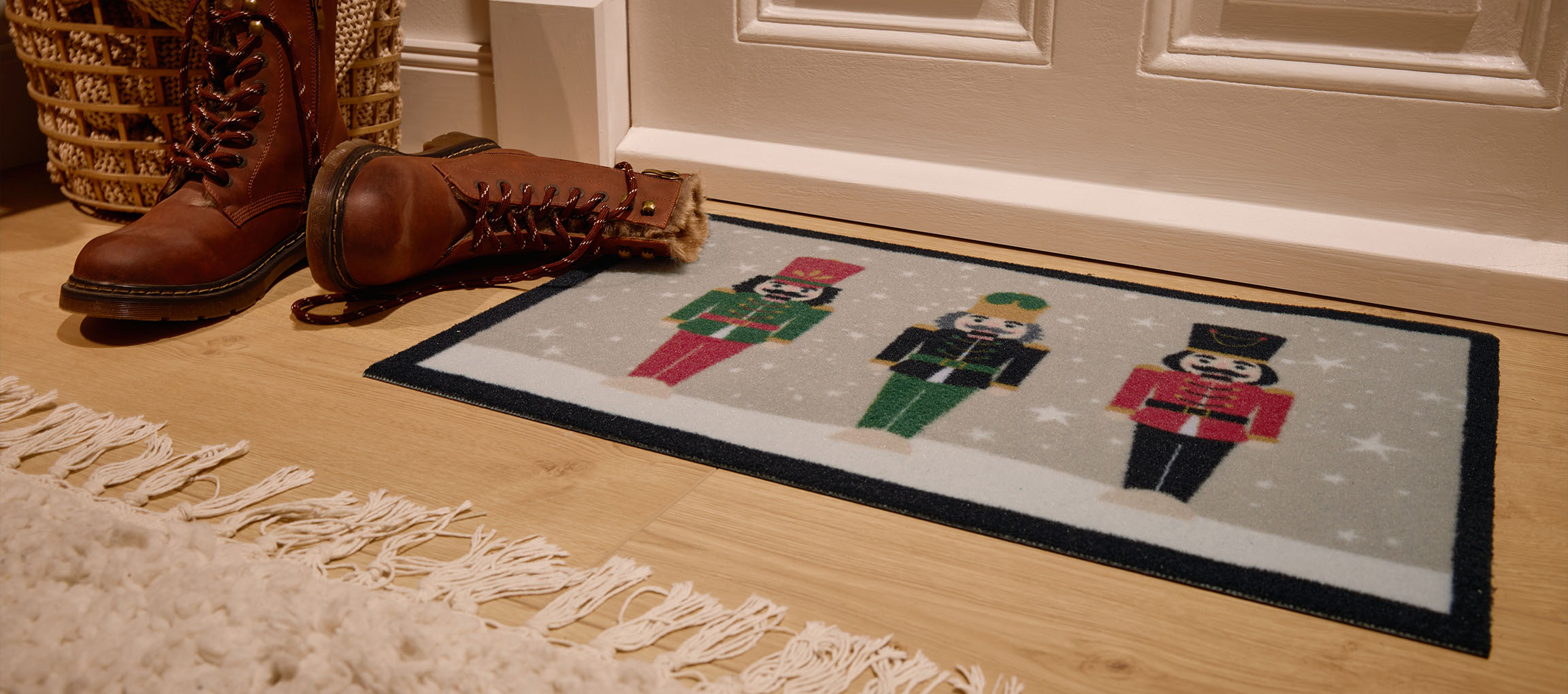 Božični predpražnik z louskáčki, rjavi škornji in pletena košara pri vhodu.