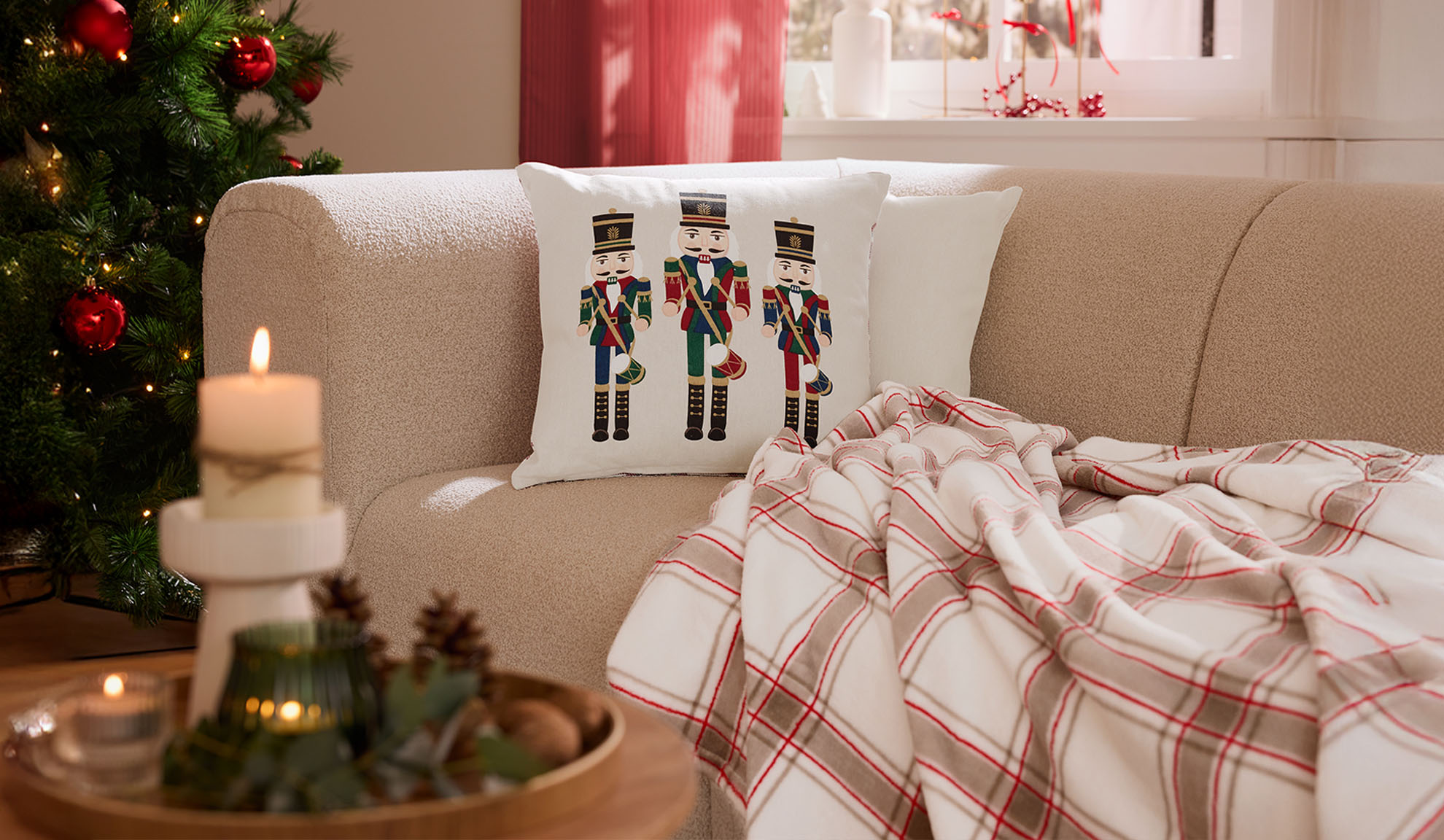 Božična dnevna soba s kavčem, blazinami z motivi hrestačev, karirasto odejo in svečami.