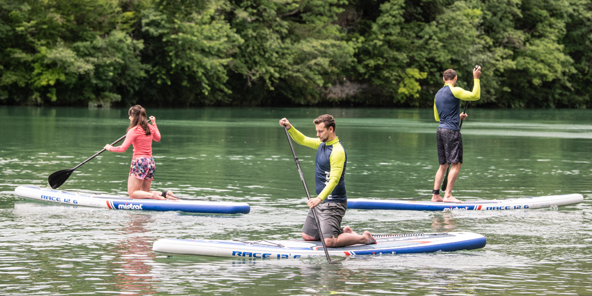 Tri osebe se vozijo s sup deskami Mistral Race 12'6 na jezeru.
