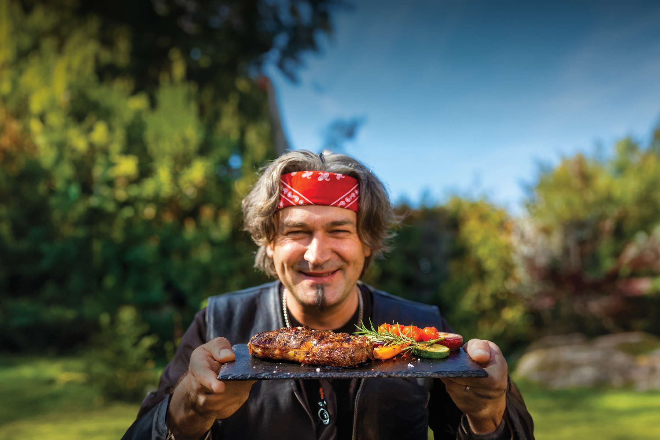 Moški drži krožnik z zrezkom in zelenjavo na prostem.