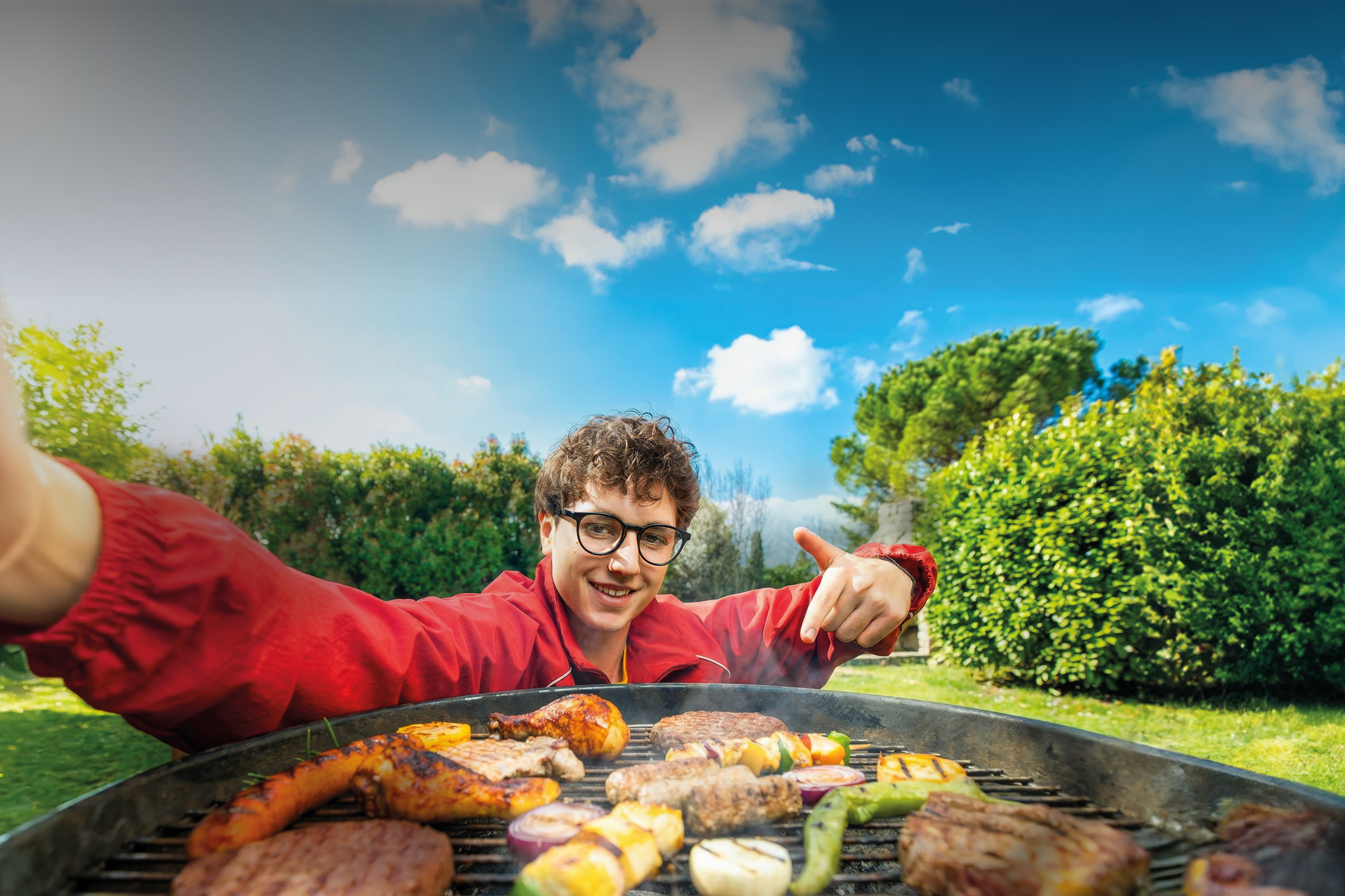 Moški peče na žaru meso, zelenjavo in sire, s širokim nasmehom kaže na hrano.