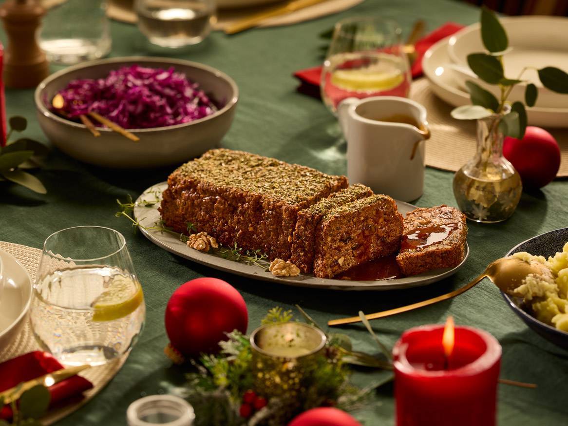 Praznična miza z mesno štruco, rdečim zeljem in božičnimi okraski.