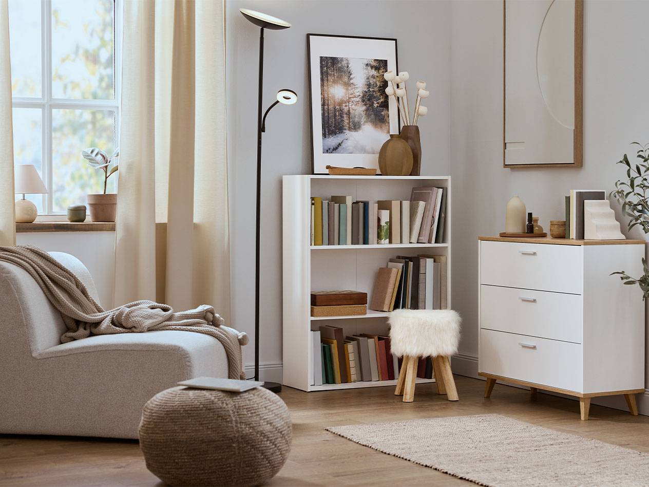 Udobna dnevna soba z naslanjačem, knjižno polico in komodo v nevtralnih barvah.