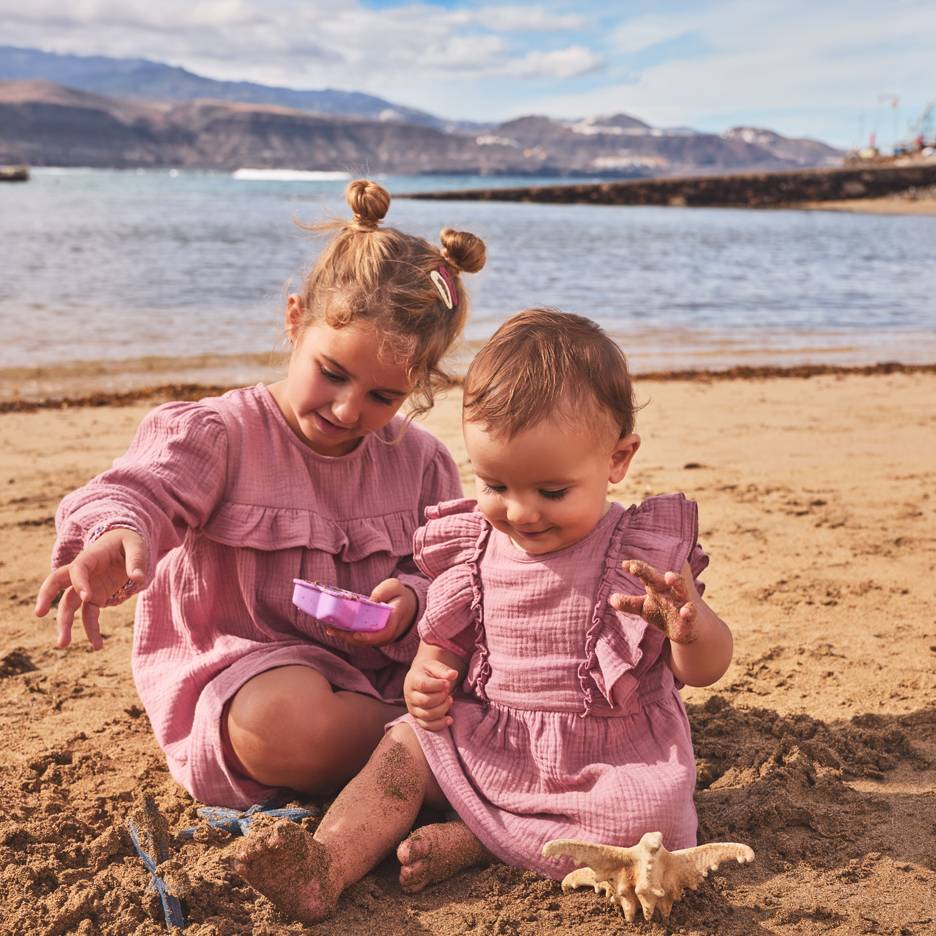 Dve deklici v rožnatih oblekah se igrata v pesku na plaži.